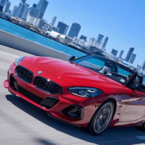 Red BMW Z4 convertible driving on a road with a city skyline in the background.