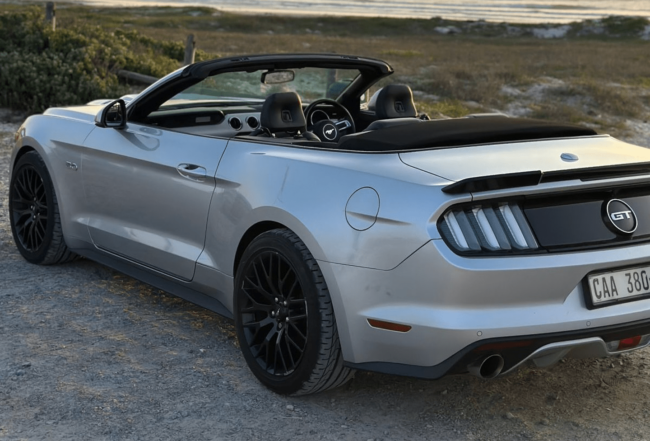 Silver Ford Mustang GT convertible parked with the top down, showcasing its sleek design.